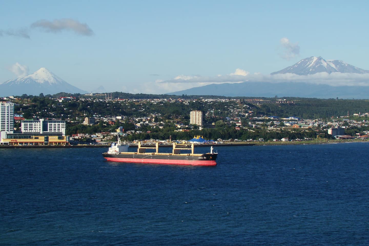 Puerto Montt visto desde la bahía, con un buque de carga en primer plano y los volcanes Osorno y Calbuco al fondo